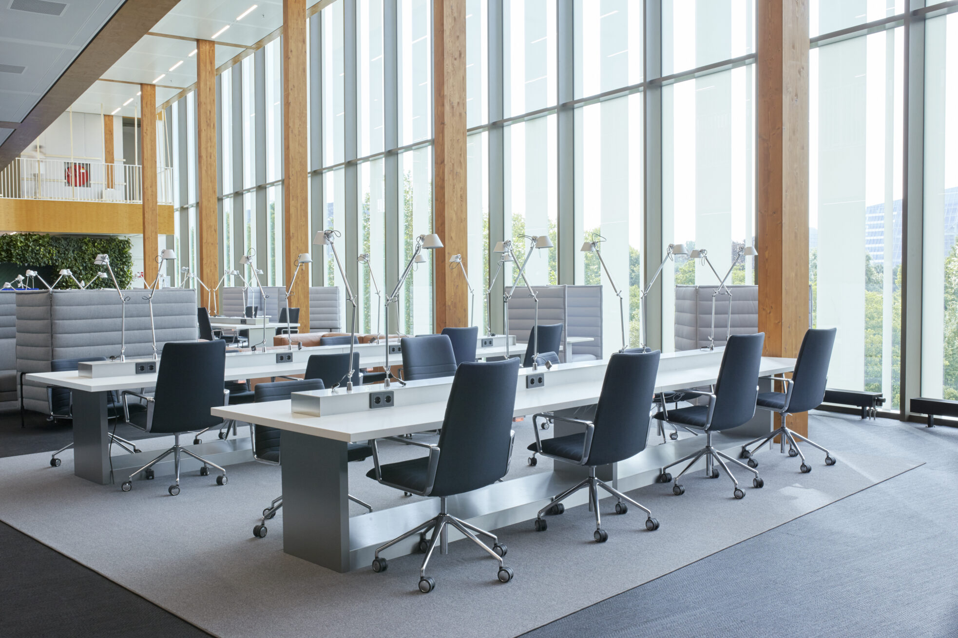 Open werkruimte met hoge glasgevel, lange witte werktafels en donkerblauwe bureaustoelen