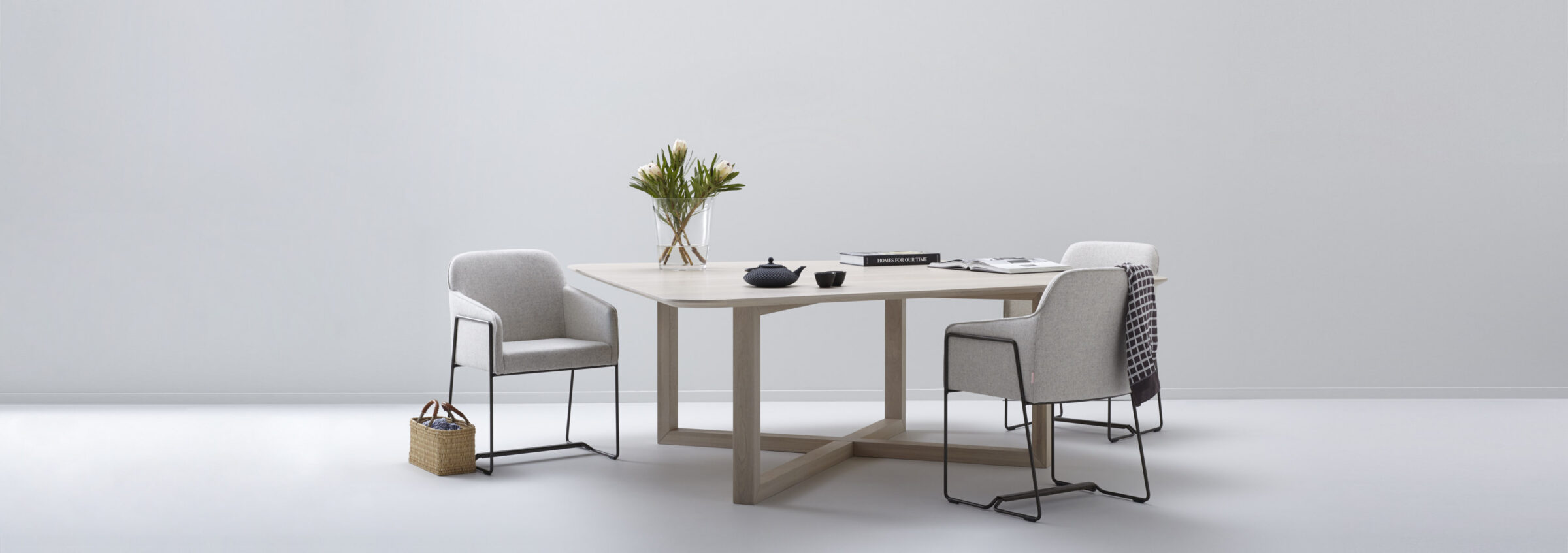Licht houten tafel STONE met onderstel van kruisende balken en drie lichtgrijze fauteuils in een lichte studio