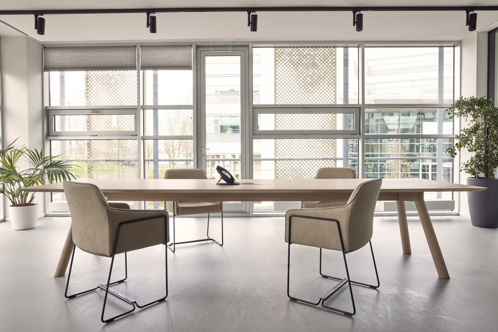 Lichte vergaderruimte met een lange eiken tafel en vier beige fauteuils met zwart draadframe
