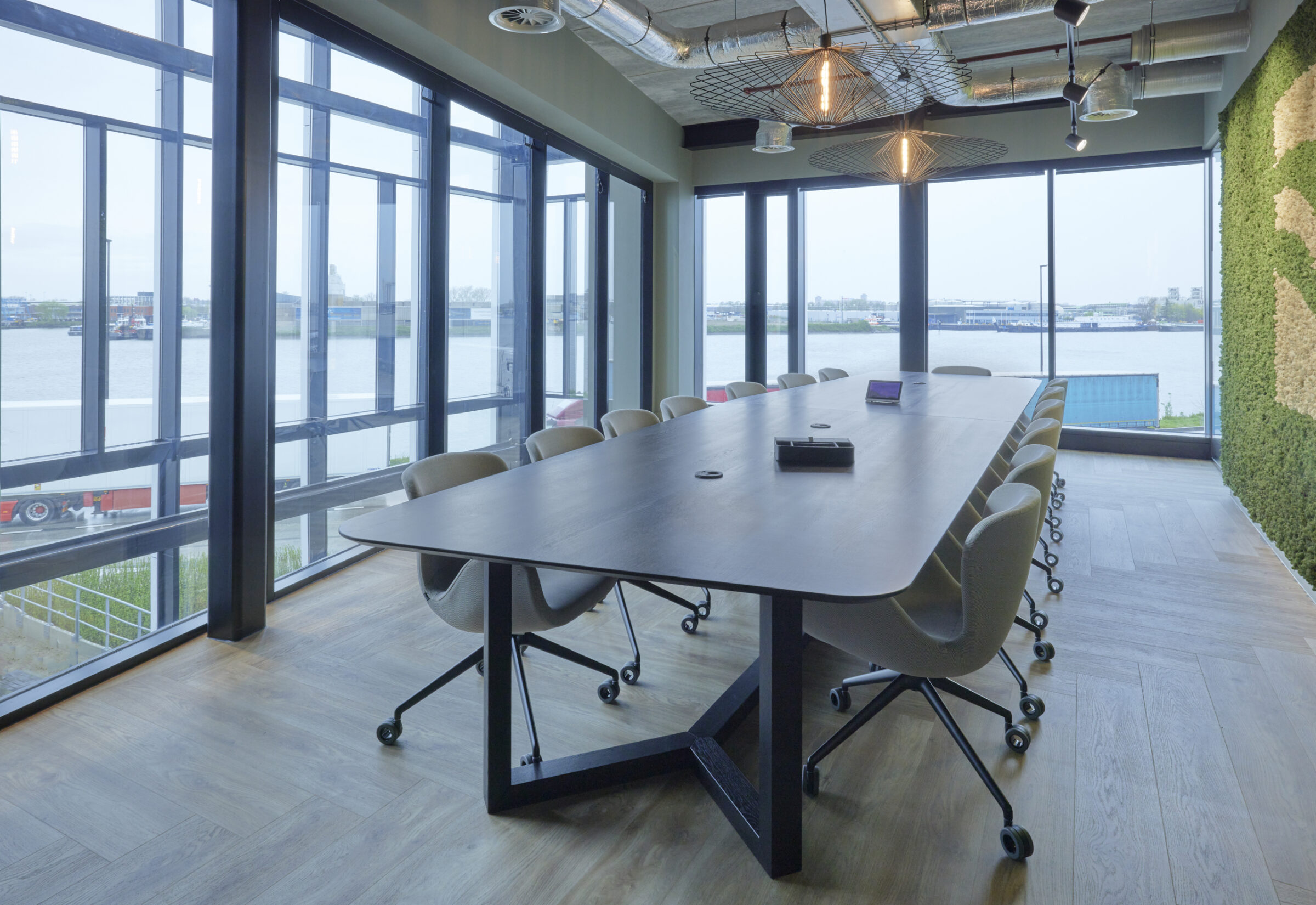 Lange vergadertafel met donker blad en beige stoelen voor een glazen gevel met uitzicht op de rivier