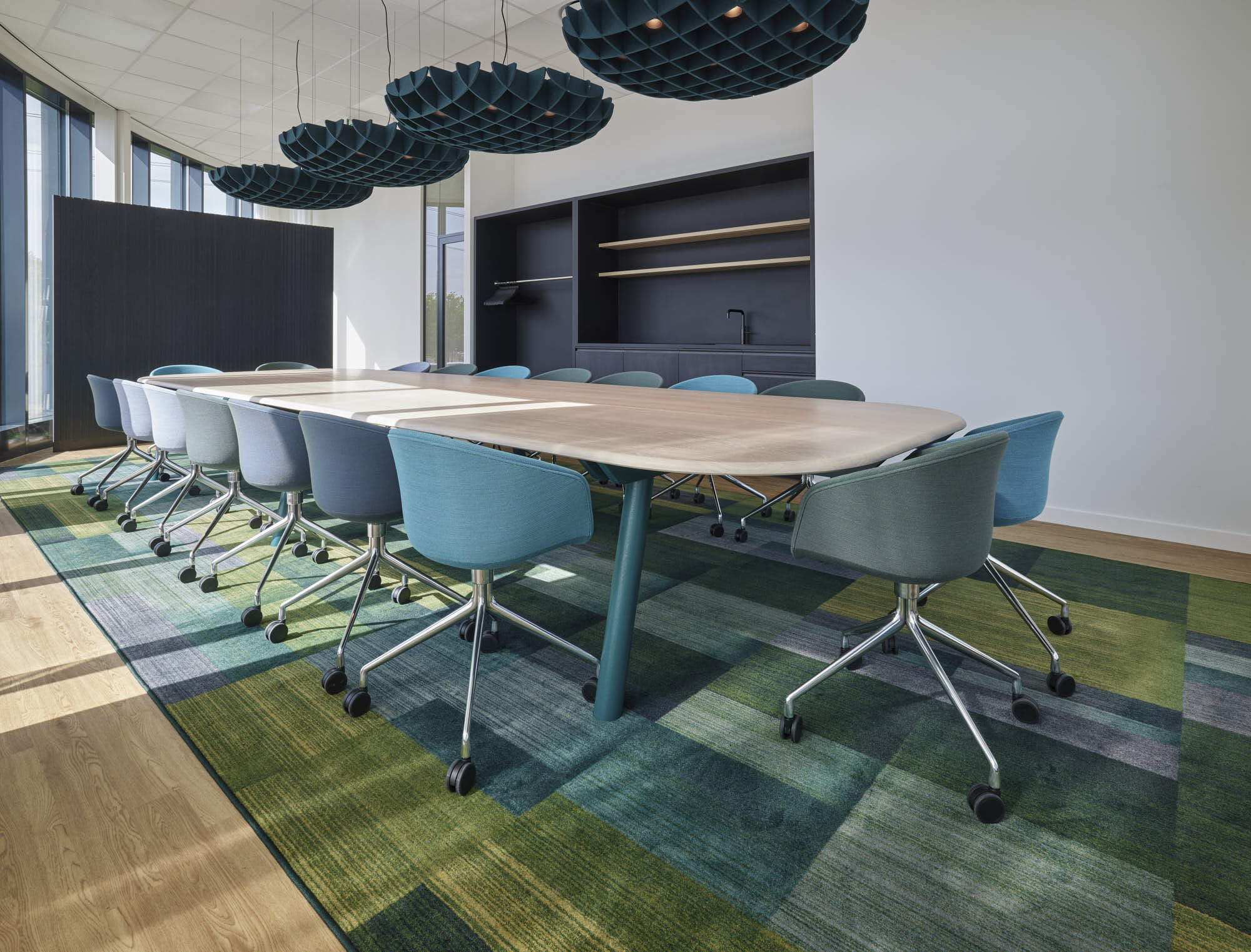 Vergaderzaal met een lange tafel met licht houten blad en blauwgroene kuipstoelen