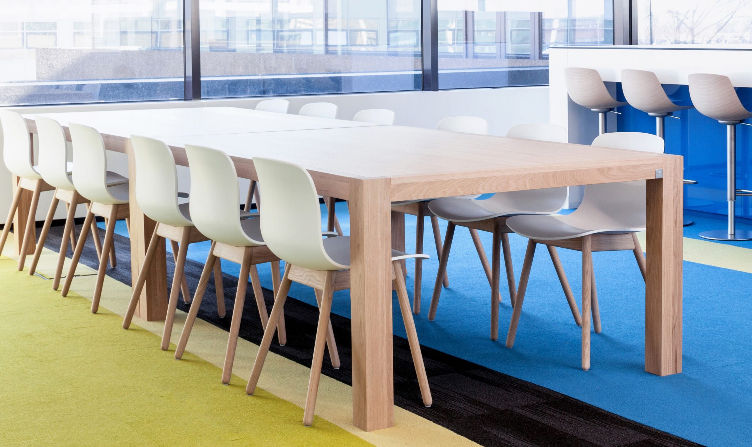 Lichte werkruimte met lange tafels van licht massief hout en witte kuipstoelen